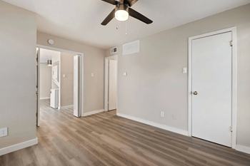 an empty living room with a ceiling fan and a door to a hallway
